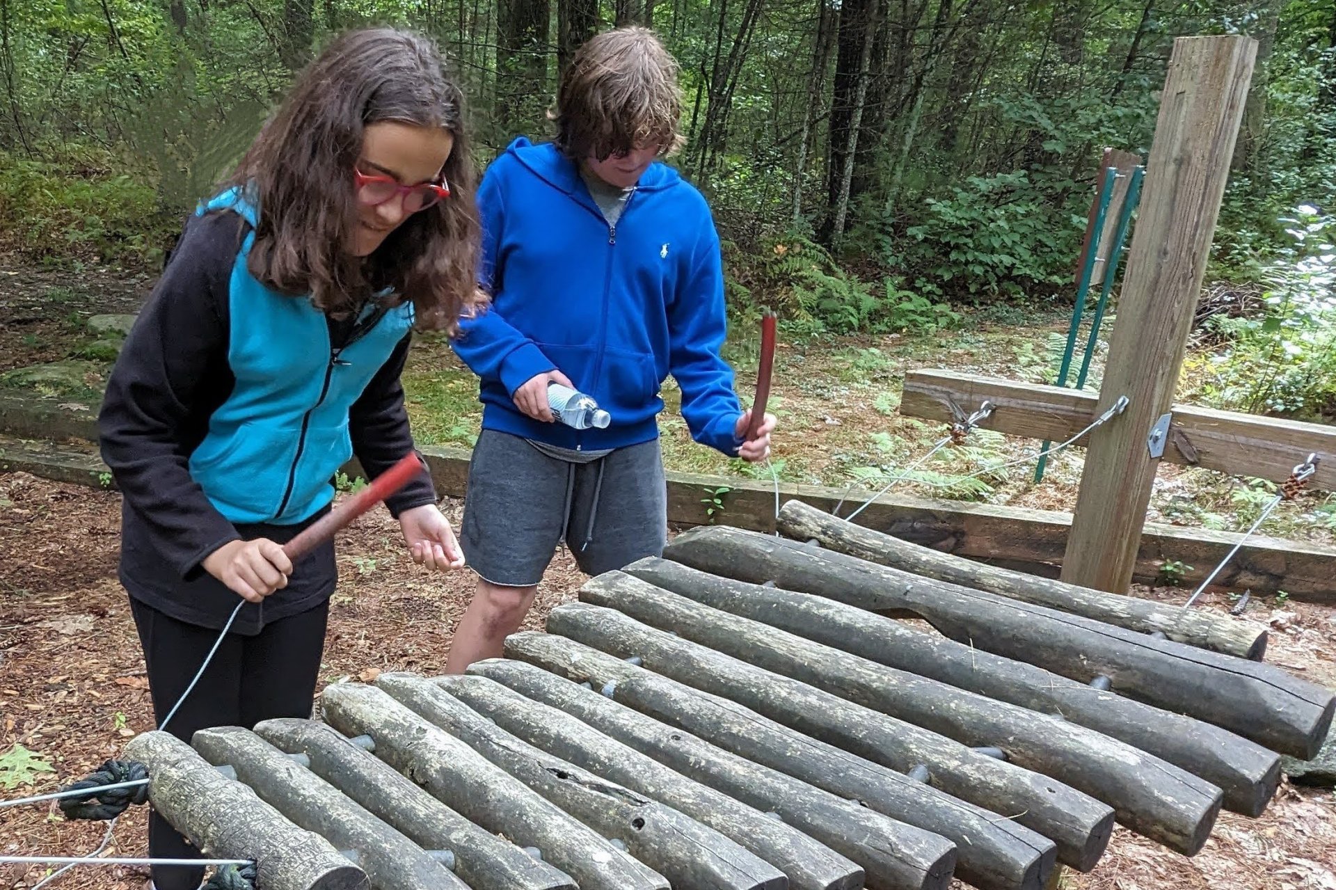 Students play xylophone made of logs outdoors