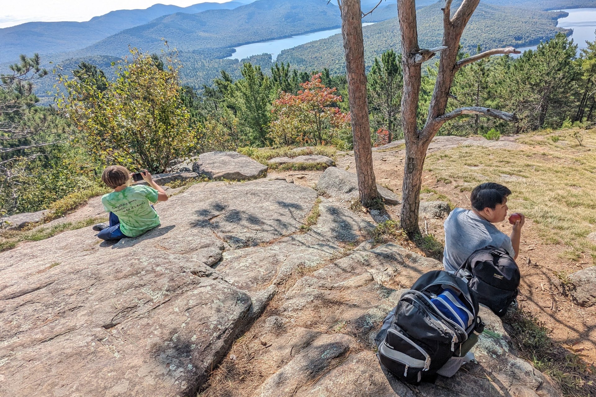 Two boys sitting on the top of a hill looking at the surrounding mountains.
